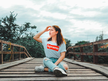 Full length of woman sitting on bridge against sky