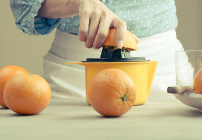 Midsection of woman making juice of orange on table