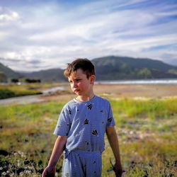 Cute boy standing on land against cloudy sky