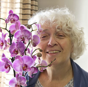 Senior woman holding a lilac orchid and smiling at the camera