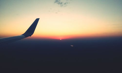 Airplane wing against sky during sunset