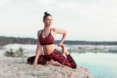 Young woman sitting on shore against sky