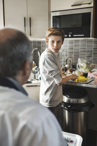 Boy looking at father while cutting vegetables in kitchen
