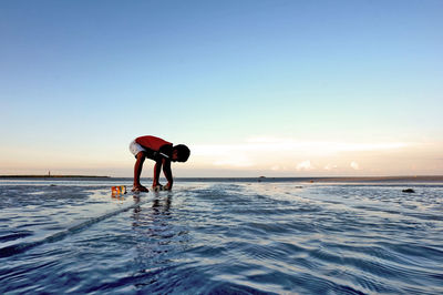 Boy playing on sea shore at beach against clear sky during sunset