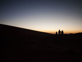 Silhouette people standing in desert against clear sky