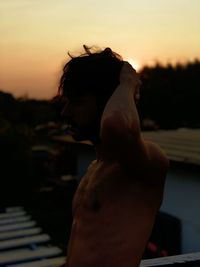 Side view of shirtless woman standing against sky during sunset