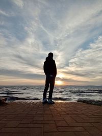 Rear view of man standing on beach during sunset