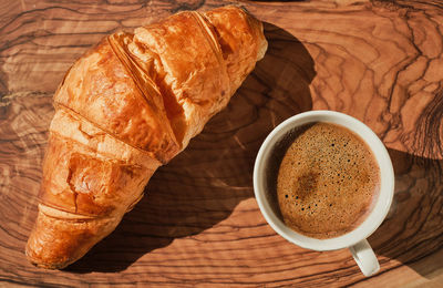 Coffee and croissant on wooden table, french breakfast idea, sunny bright day. 