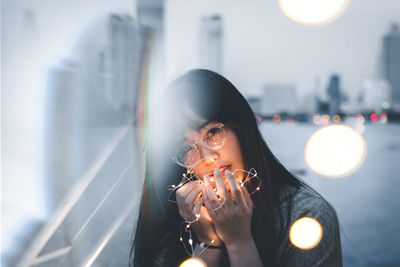 Portrait of woman holding illuminated string lights in city