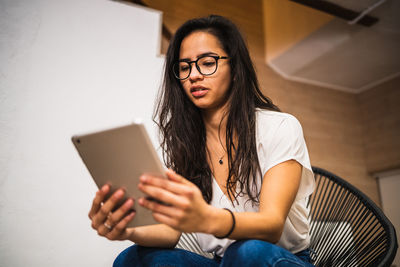 Young woman using mobile phone while sitting on laptop