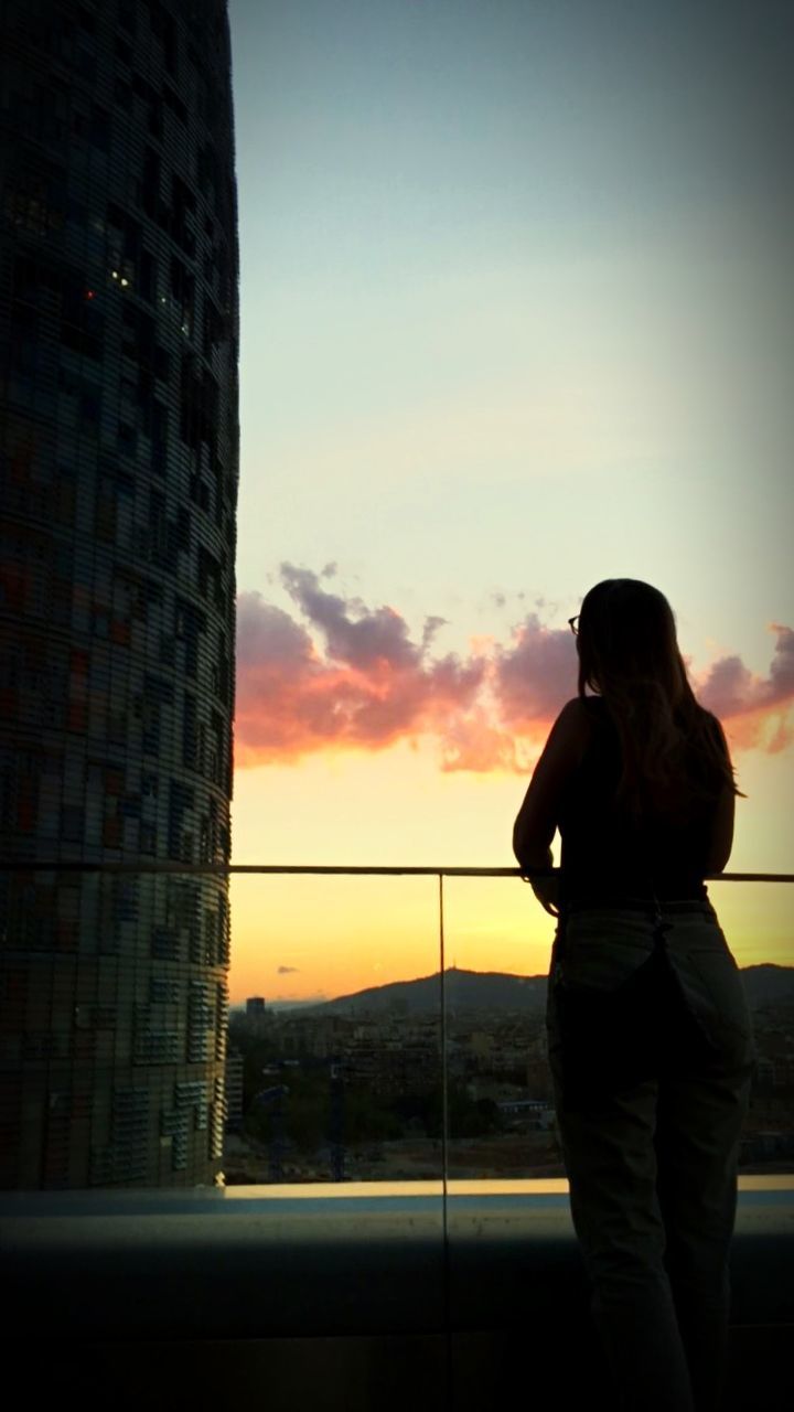 sky, sunset, one person, silhouette, standing, real people, lifestyles, three quarter length, architecture, building exterior, leisure activity, built structure, nature, rear view, city, women, orange color, adult, outdoors, looking at view, hairstyle