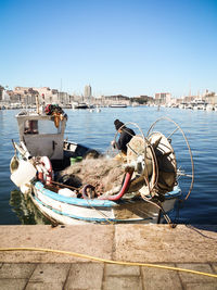 Fisherman with net on boat at harbor against clear blue sky