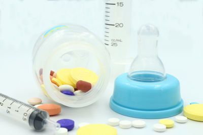 Close-up of medicines spilling from baby bottle with syringes on blue background