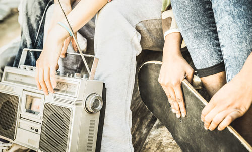 Midsection of friends holding skateboard and radio while sitting outdoors