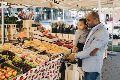 Father carrying daughter while buying fruit and vegetables in market