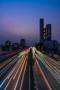 Light trails on road amidst buildings against sky at night