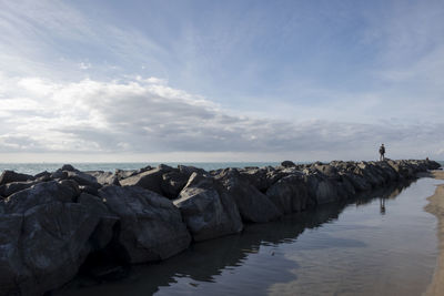 Rocks on shore by sea against sky