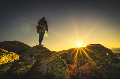 Silhouette man standing on rock against sky during sunset