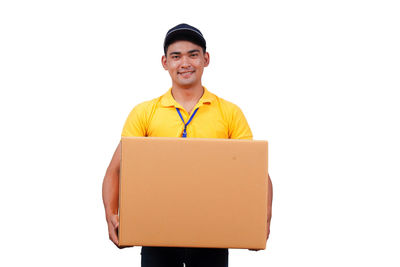 Portrait of smiling delivery man standing with cardboard box against white background