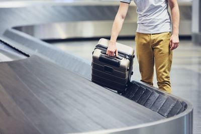 Midsection of man picking suitcase from conveyor belt