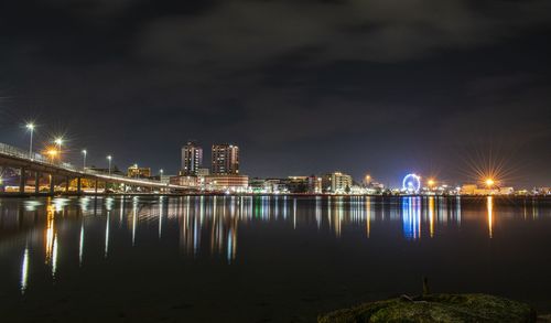 Illuminated buildings by river against sky at night