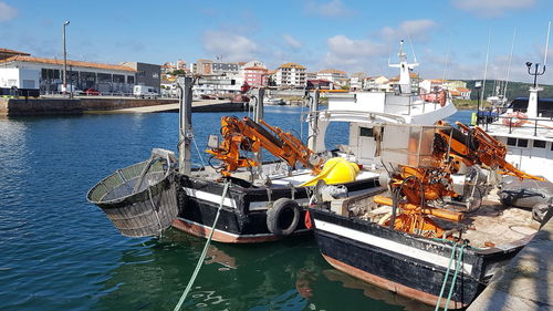 Fishing boats moored at harbor against sky