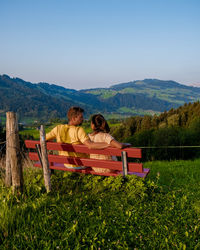 Rear view of couple sitting on bench against sky