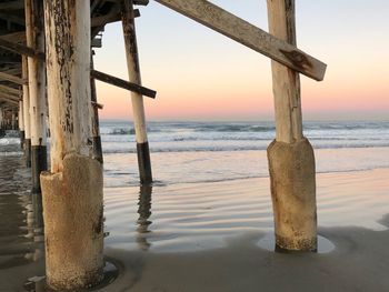 Wooden posts on beach against sky during sunset