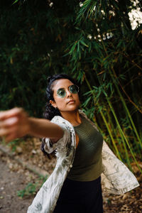 Portrait of young woman wearing sunglasses standing by tree