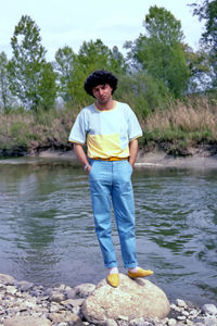 Portrait of young man standing on rock against lake