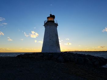 Lighthouse by sea against sky at sunset