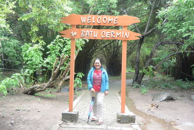 Full length of boy standing by sign against trees