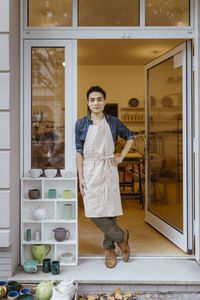 Confident male owner with hand on hip standing at doorway of pottery shop