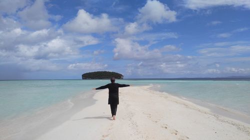 Rear view of woman with arms outstretched standing on shore at beach