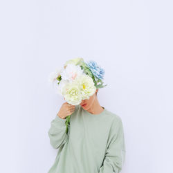 Woman holding flowers in front of face against white background