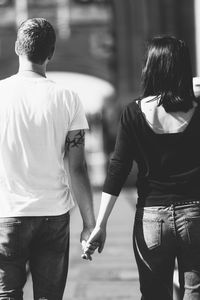 Rear view of young couple holding hands while walking on street