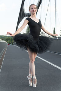 Female ballet dancer dancing on bridge against sky