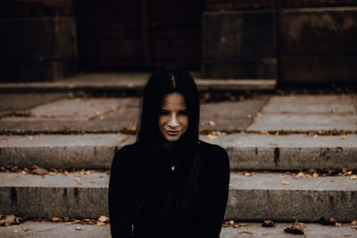 Young woman looking down while standing against staircase