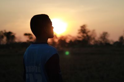 Thoughtful teenage boy standing against sky during sunset