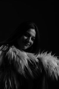 Close-up of woman wearing fur coat against black background