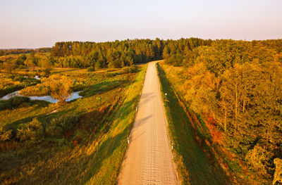 Dirt road along trees and landscape against sky