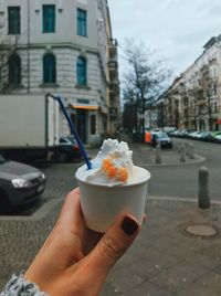 Hand holding ice cream cone on street in city