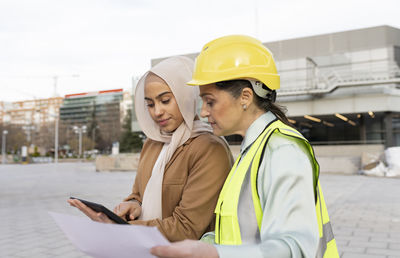 Young businesswoman sharing tablet pc with architect wearing hardhat