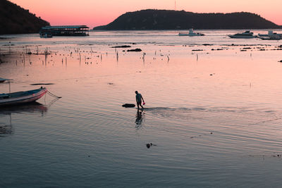 Man standing in sea against sky during sunset