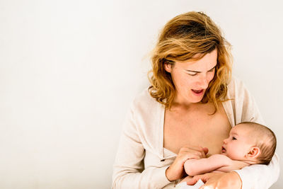 Mother breastfeeding baby against white background