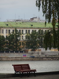 Bench by river against buildings in city