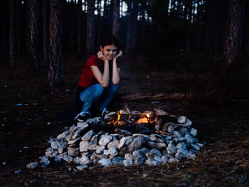 Full length of man sitting on log in forest