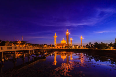 Illuminated building by lake against sky at night