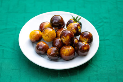 Fresh cherry tomatoes of different varieties on a plate on the blurred background, close-up