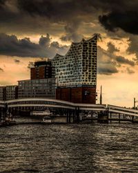 Bridge over river by buildings against sky during sunset